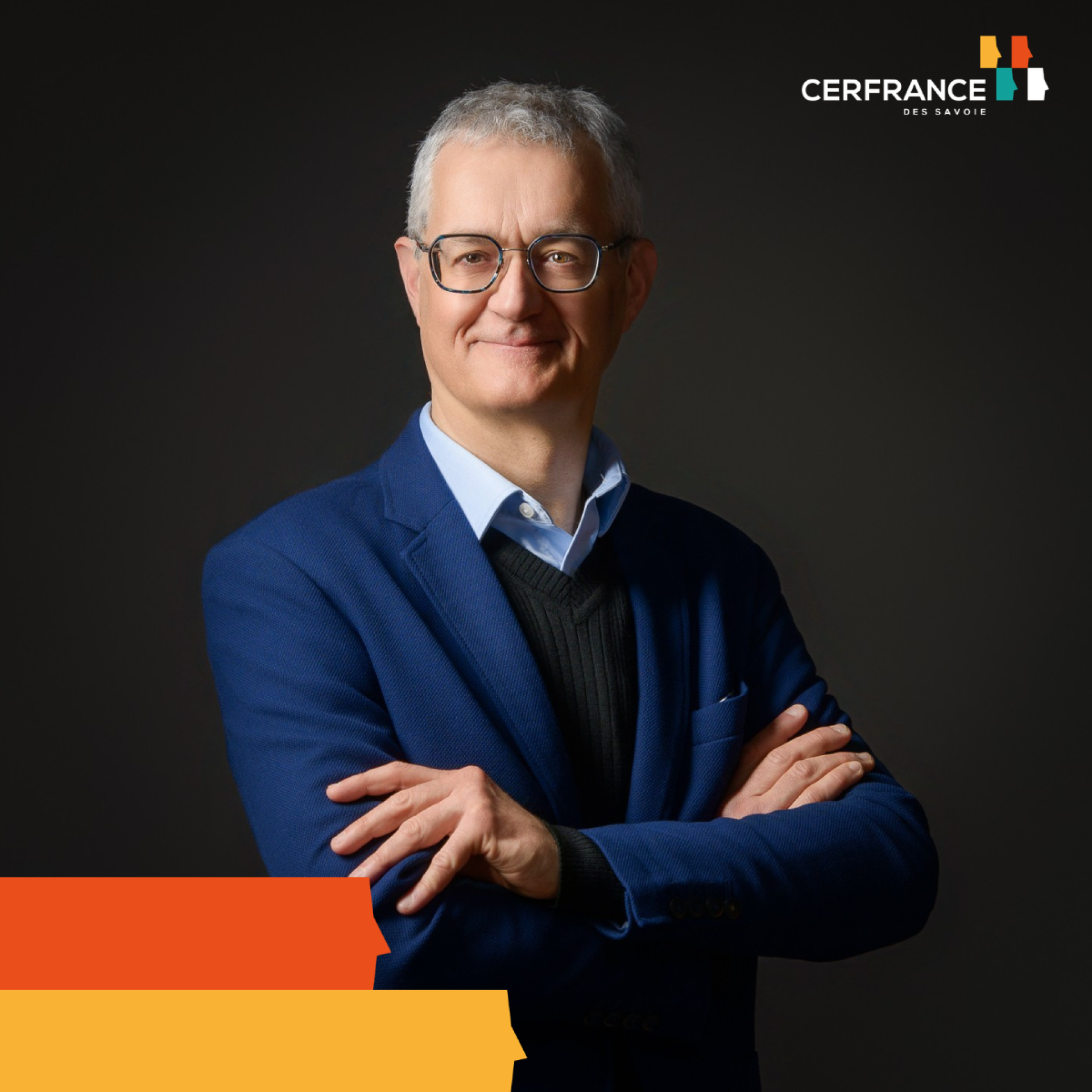 Portrait d'un homme à lunettes, bras croisés, portant une veste bleue sur un fond sombre.