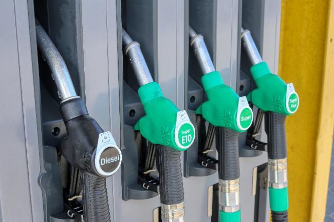 Quatre pistolets de pompe à essence alignés dans une station-service, comprenant un pistolet noir pour le Diesel et trois pistolets verts pour le Super E10, le Super et le Super Plus